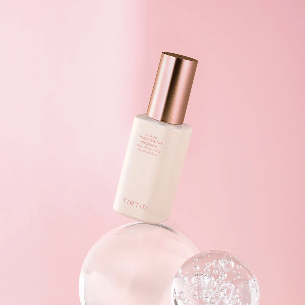 Kuva näyttää pullon "TIRTIR MASK FIT TONE UP ESSENCE" SPF30 PA++:lla vaaleanpunaista taustaa vasten, mikä antaa pehmeyden ja naisellisuuden tunteen.