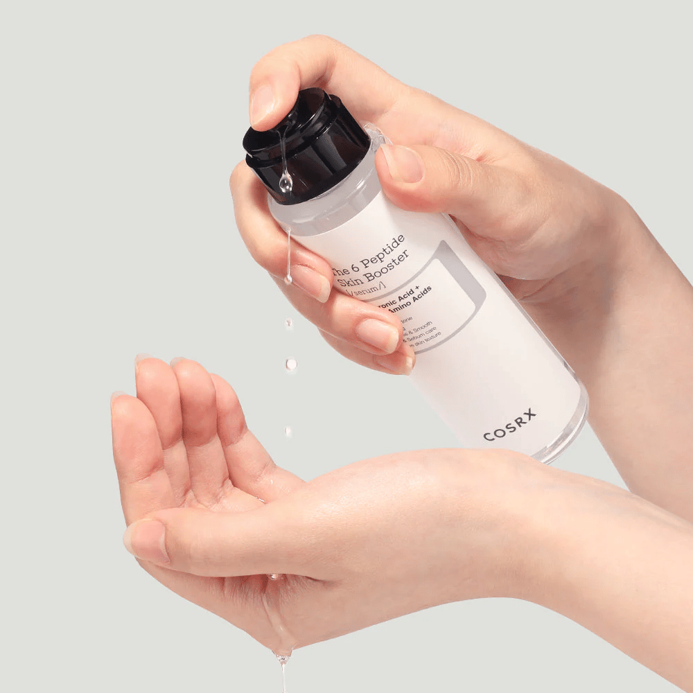 Kädet, jotka kaatavat ihonhoitotuotetta läpinäkyvästä pullosta, jossa on teksti "The Peptide Skin Booster".