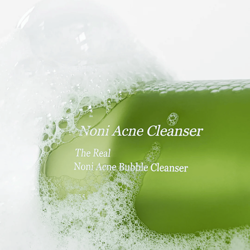 Pullo, jossa on The Real Noni Acne Bubble Cleanser, on keskipisteessä ja ympäröity runsaalla vaahdolla. Raikas vihreä väri viestii luonnollisista ainesosista, täydellinen puhdistukseen ja aknen torjuntaan. Ihanteellinen tuote puhtaalle ja kirkkaalle iholle.