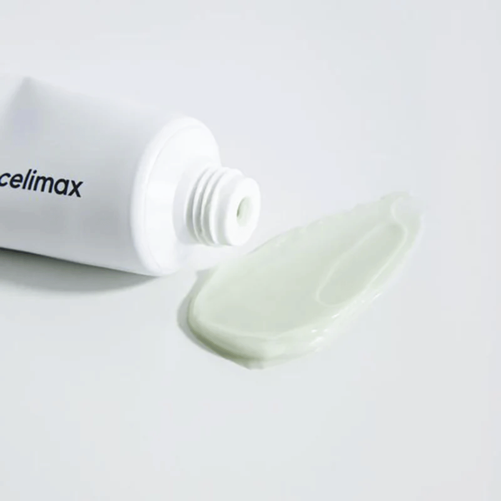 Celimax Noni Energy Repair Cream valkoisessa tuubissa, ja pieni määrä vaaleanvihreää voidetta on puristettu tuubin viereen valkoiselle pinnalle. Voide on tarkoitettu ravitsemaan ja korjaamaan ihoa.