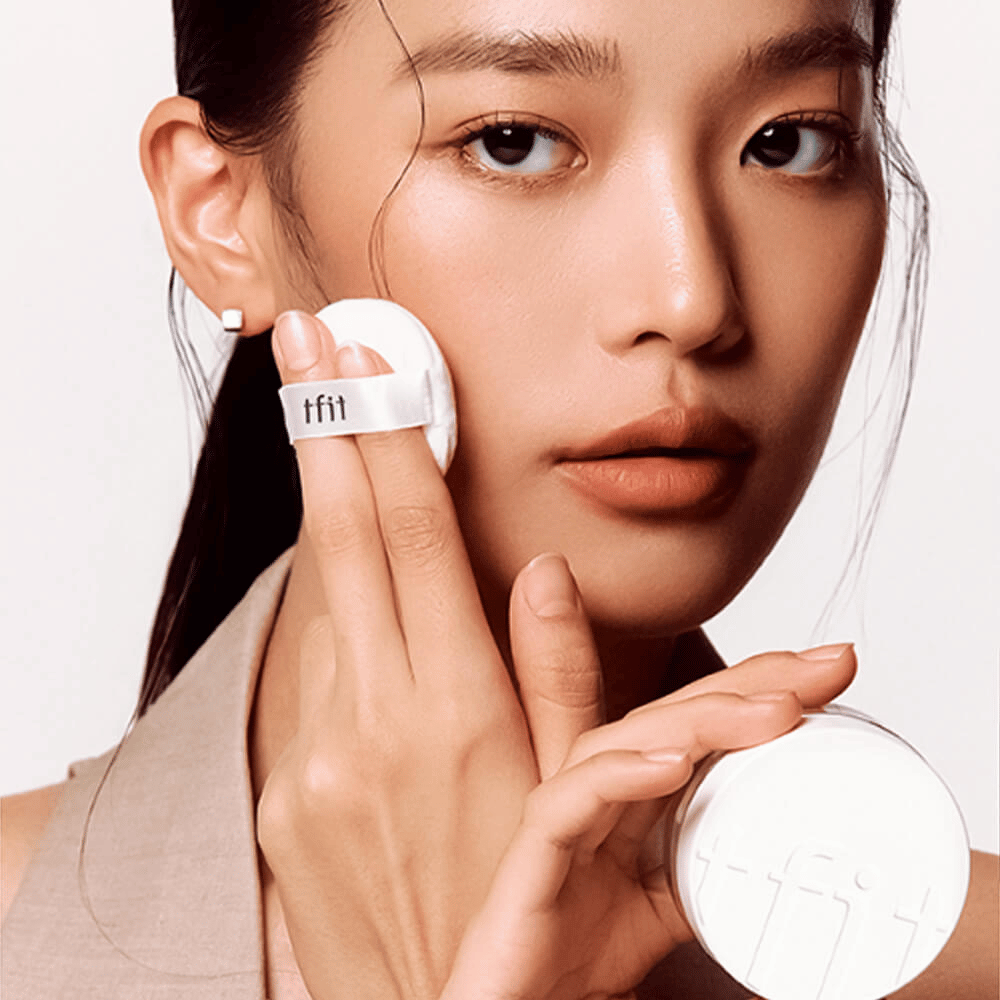 Nainen levittää TFIT Translucent Set Finishing Powder #02 Skin Beige puffilla, pitää valkoista puuteripurkkia, jossa on TFIT-logo.