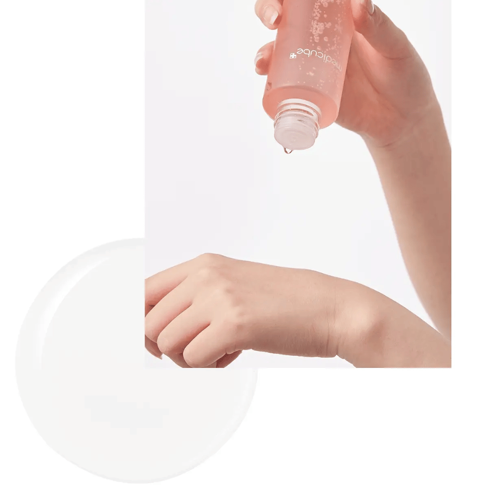Käsi kaataa Medicube Triple Collagen Toner 4.0 -kasvovettä vaaleanpunaisesta pullosta iholle, näyttää kosteuttavan koostumuksen.
