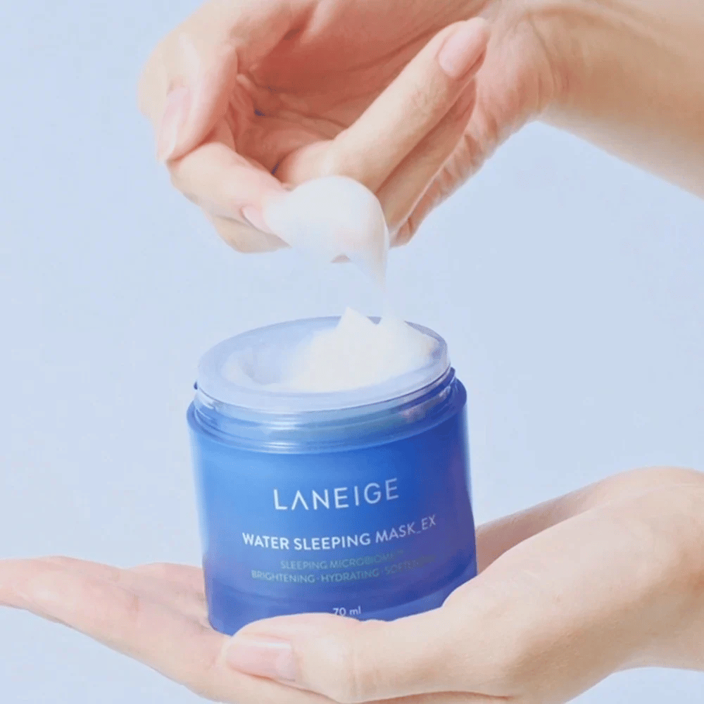 Käsi kauhoo LANEIGE Water Sleeping Mask sinisestä purkista, keskittyen hyytelömäiseen koostumukseen vaaleansinistä taustaa vasten.
