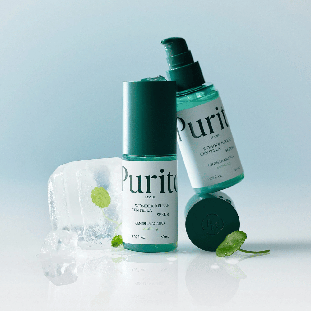 Kaksi pulloa Purito Wonder Releaf Centella Serum, yksi pystyssä ja yksi makuulla, ympäröitynä jääpaloilla, joiden sisällä on centellalehtiä, sekä irrallinen lehti vaaleansinisellä pinnalla.