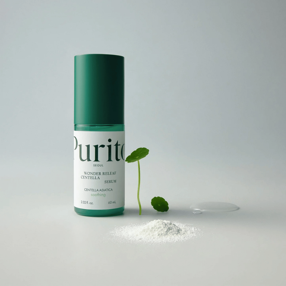Vihreä pullo Purito Wonder Releaf Centella Serum 60 ml seisoo valkoisella alustalla, ympäröitynä centellalehdillä, läpinäkyvällä seerumitipalla ja pienellä valkoisella jauheella.