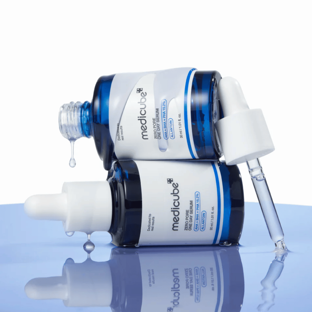 Kaksi sinistä pulloa Medicube Zero Pore One Day Serum makaamassa vastakkain, pipeteillä ja seerumitipoilla heijastavalla sinisellä pinnalla.