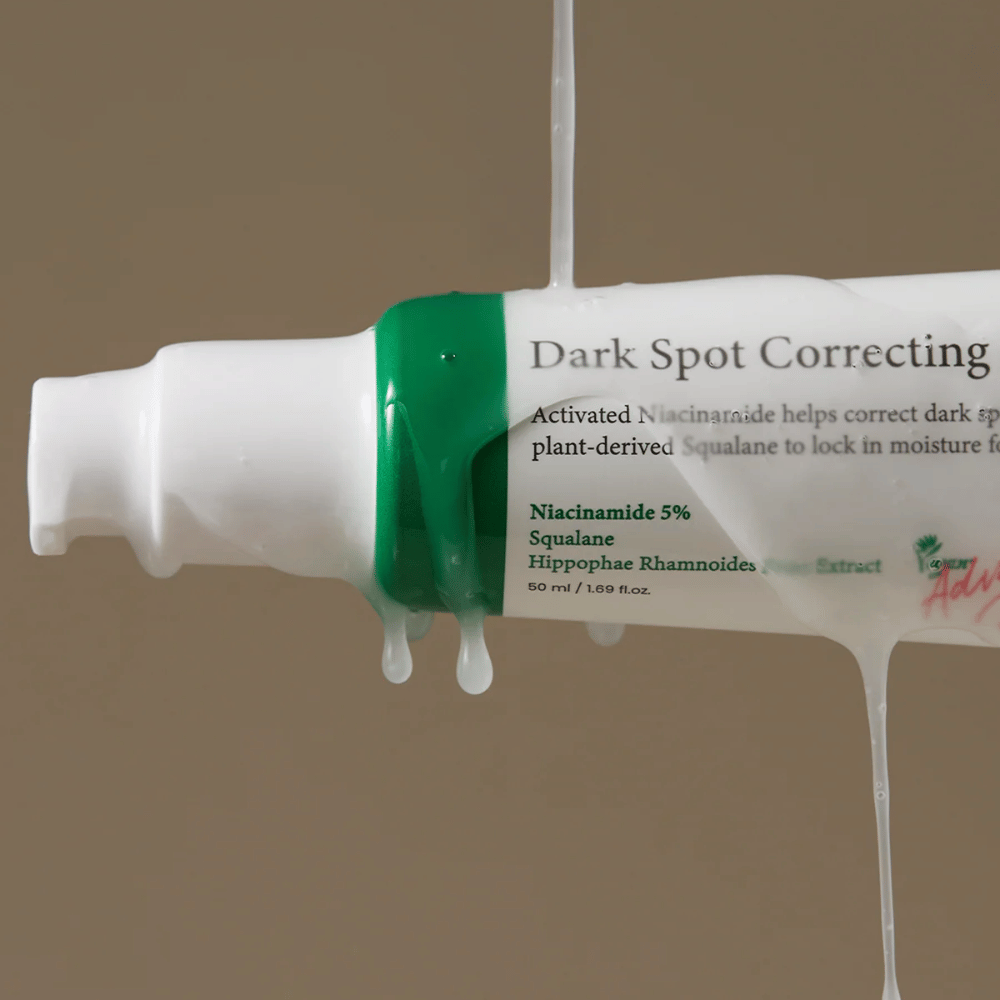 Lähikuva Axis-Y Dark Spot Correcting Glow Serum pumppupullosta, jossa on valkoinen pakkaus ja vihreä korkki, peitettynä valuvalla läpinäkyvällä nesteellä.