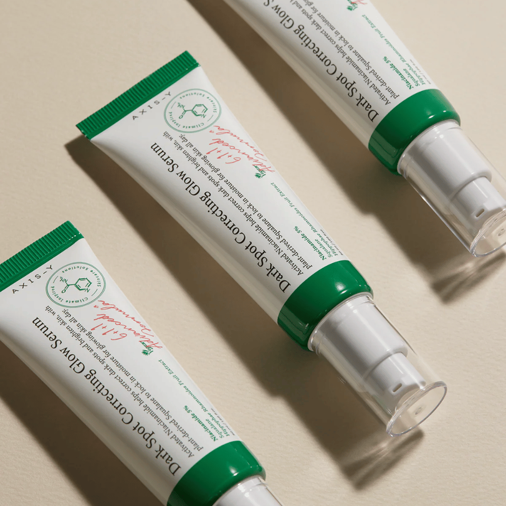 Kolme tuubia Axis-Y Dark Spot Correcting Glow Serum vihreällä korkilla ja valkoisella pakkauksella on vaalealla alustalla.