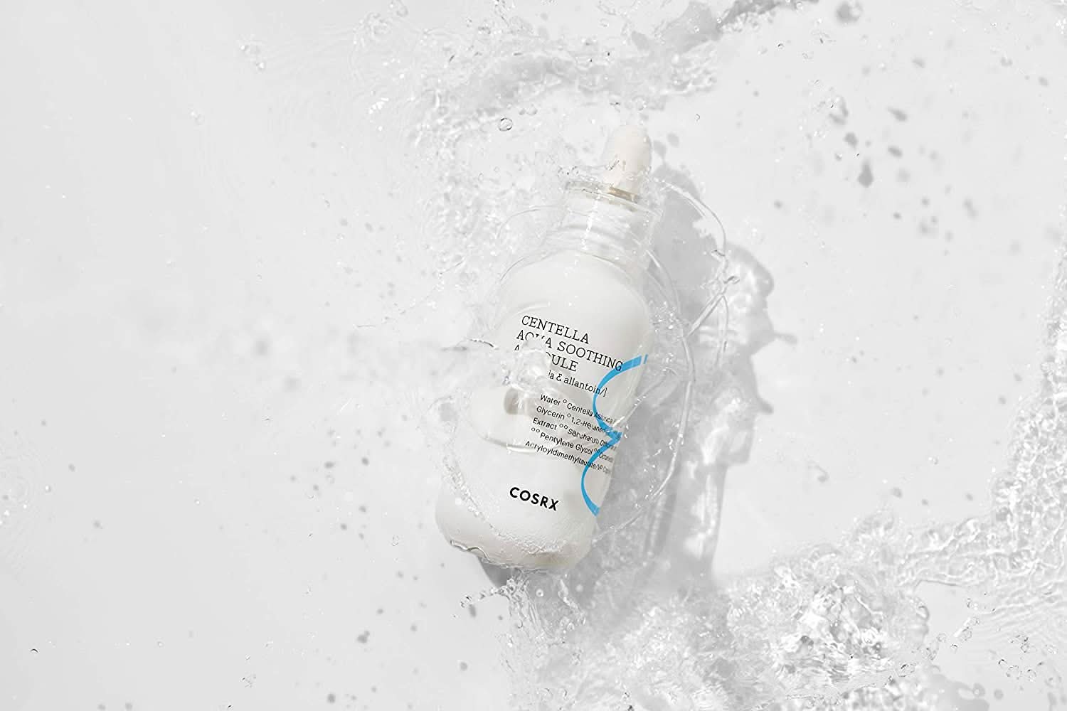 Pullo COSRX Centella Aqua Soothing Ampoule 40ml roiskuu valkoiselle pinnalle, vähentää punoitusta ja antaa rauhoittavaa kosteutusta.