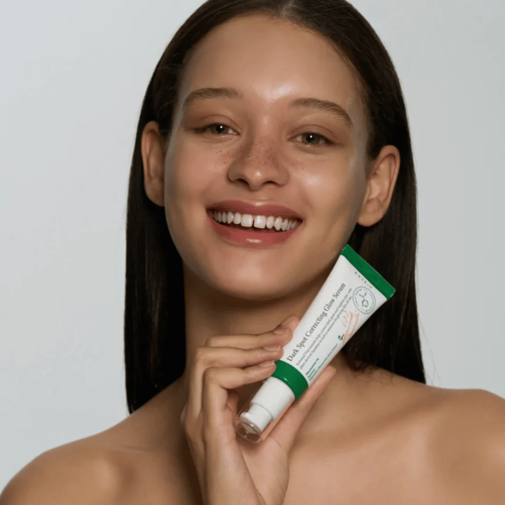 Nuori nainen pitää kädessään AXIS - Y Dark Spot Correcting Glow Serum 50 ml:n tuubia.
