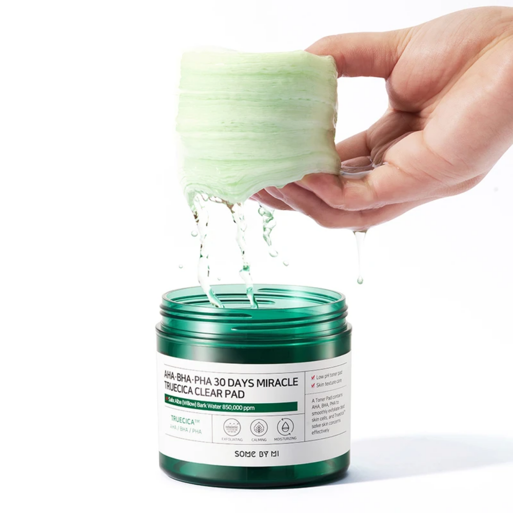 Käsi kaataa vihreää nestettä purkkiin SOME BY MI:n AHA, BHA, PHA 30 Days Miracle Truecica Clear Pad 70 kpl aknen puhkeamisen hoitoon.