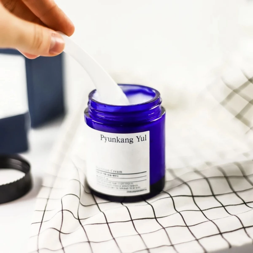 Henkilö käyttää purkkia Pyunkang Yul Nutrition Cream 100ml pöydällä.