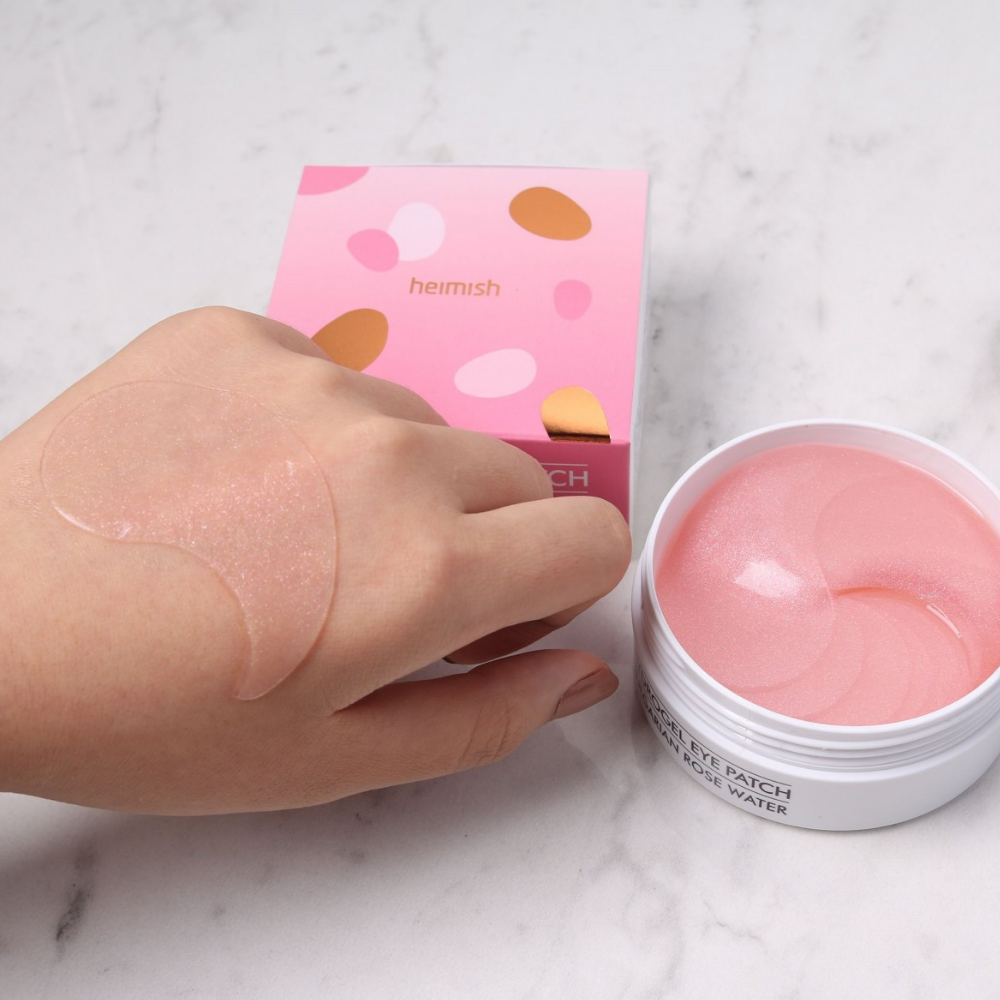 Käsi, joka pitää vaaleanpunaista Bulgarian Rose Hydrogel Eye Patch 60 kpl heimish:sta ja levittää silmänympärysnaamion.
