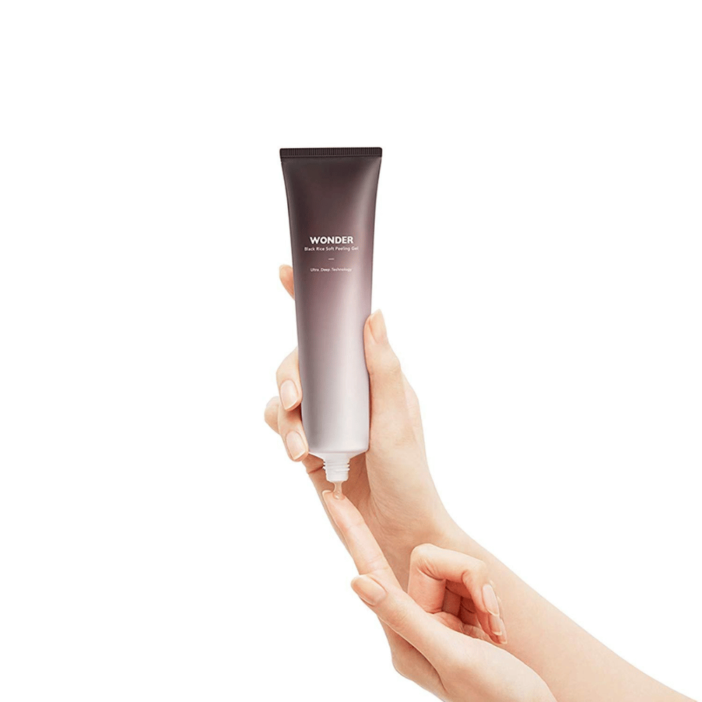 Naishenkilön käsi pitelee Haruhuru Wondersin Black Rice Soft Peeling Gel 100 ml:n putkiloa valkoisella taustalla.