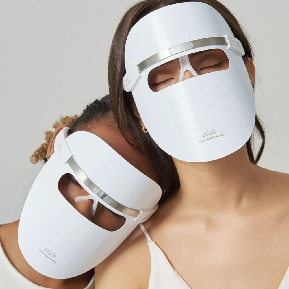 Kaksi naista, jotka käyttävät valkoisia naamioita, esittelevät ECLAIR LED Therapy Mask ihon sävyn parannuksia.