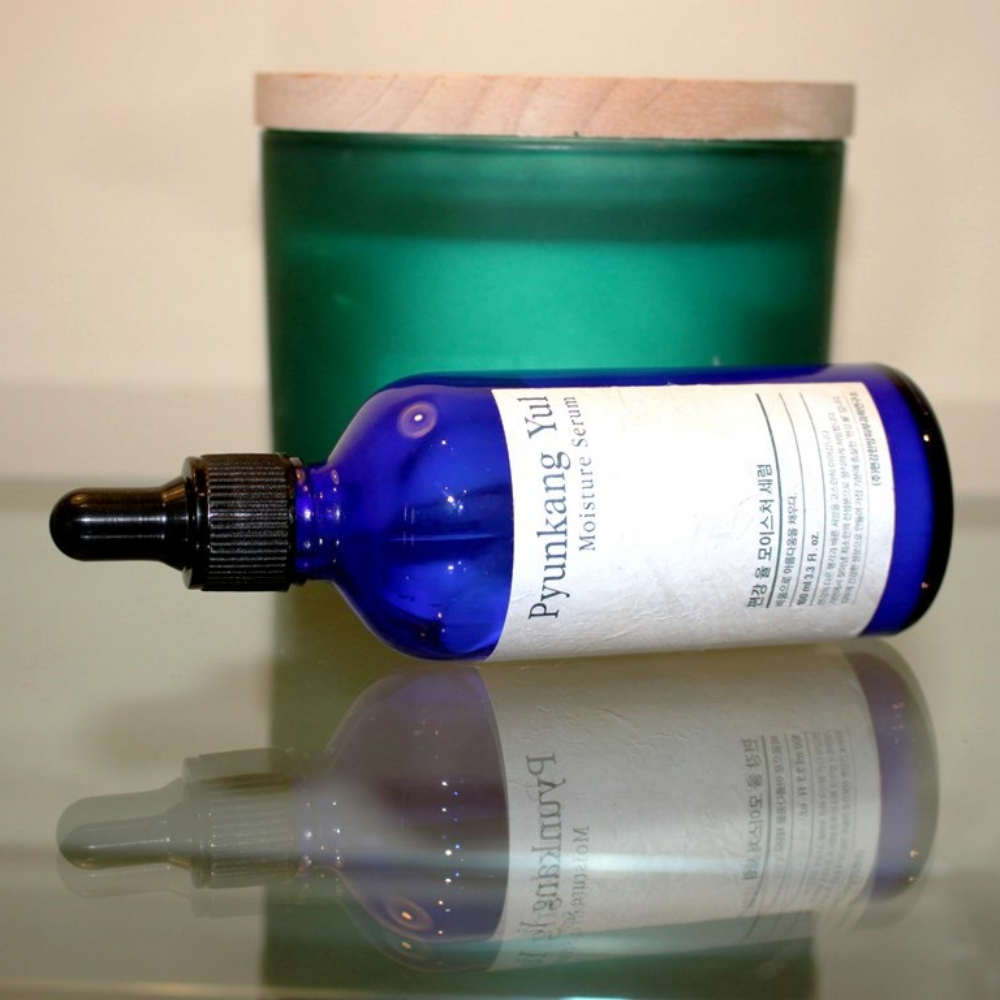 100 ml:n Pyunkang Yul Moisture Serum pullo tasapainottaa kosteustasoa pöydällä kynttilän vieressä.
