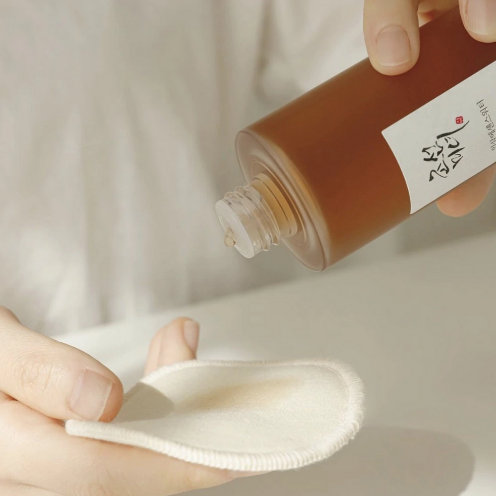 Henkilö kaataa Beauty of Joseon Ginseng Essence Water 150 ml liinaan käsitelläkseen kuivaa ihoa ja vähentääkseen talintuotantoa.
