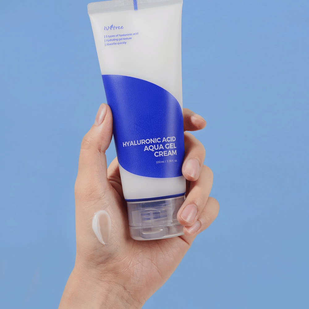 Käsi pitelee 100 ml:n tuubia Isntree Hyaluronic Acid Aqua Gel Cream sinisellä taustalla.